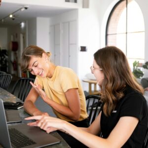 Two women engaged in a collaborative discussion at a modern office setting over laptops.