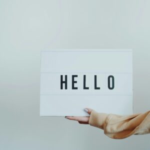 A hand holds a white sign displaying the word 'Hello' against a plain background.